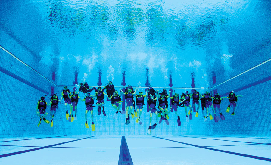 Long line of scuba divers mid water in the National Aquatic Center pool